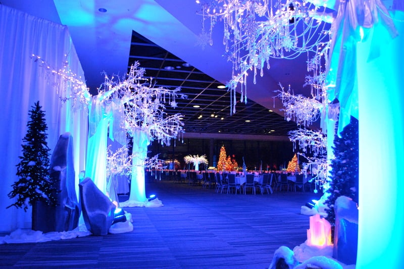 White branches, hanging crystals and blue lighting frame an entrance to a holiday reception.