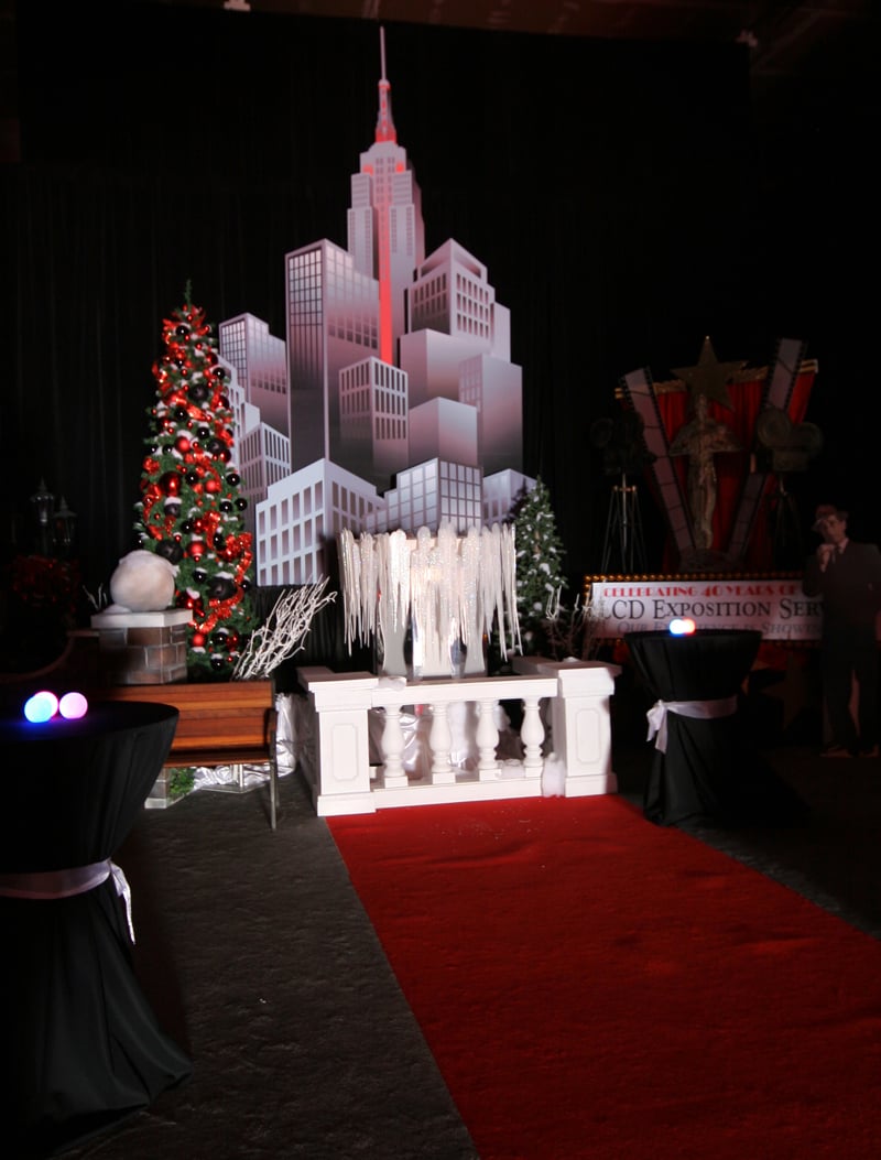 A red-carpet entrance framed by cocktail tables, holiday trees and a city skyline backdrop.