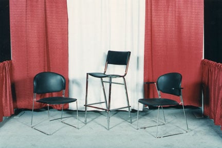 Two black sled-base chairs and a taller black barstool in a red and white draped booth.