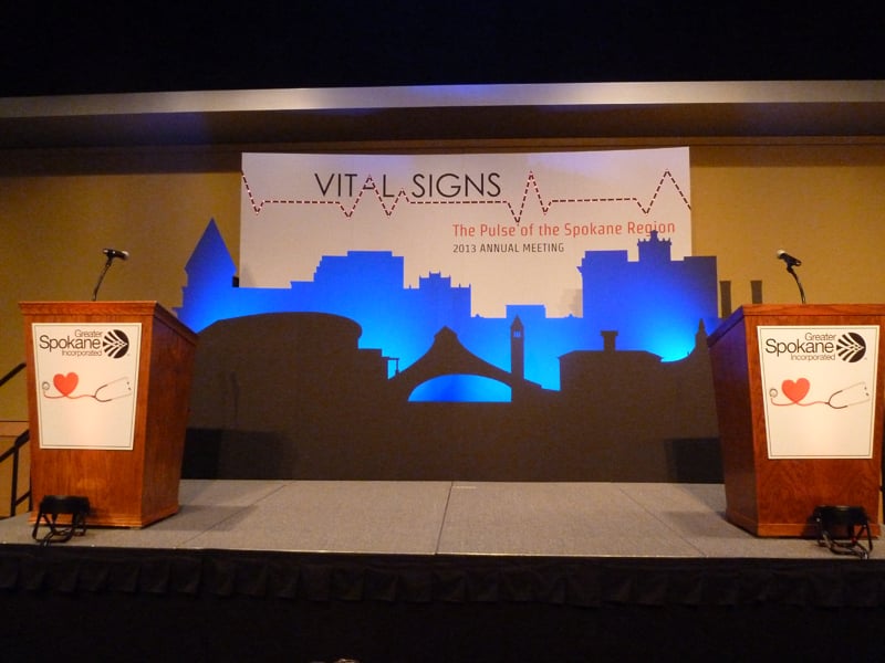 A Spokane skyline stage backdrop with blue lighting and two lecterns for the GSI annual meeting.
