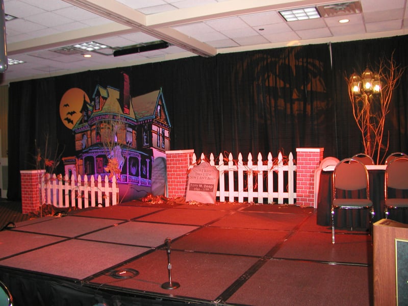 A Halloween stage set with a haunted-house backdrop, picket fencing and theatrical lighting.