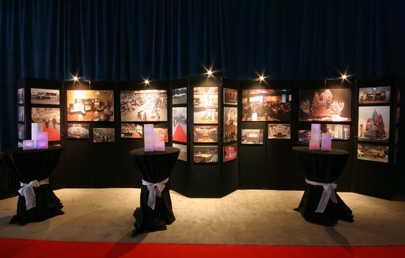Spotlit display panels showcase event photography behind black cocktail tables.