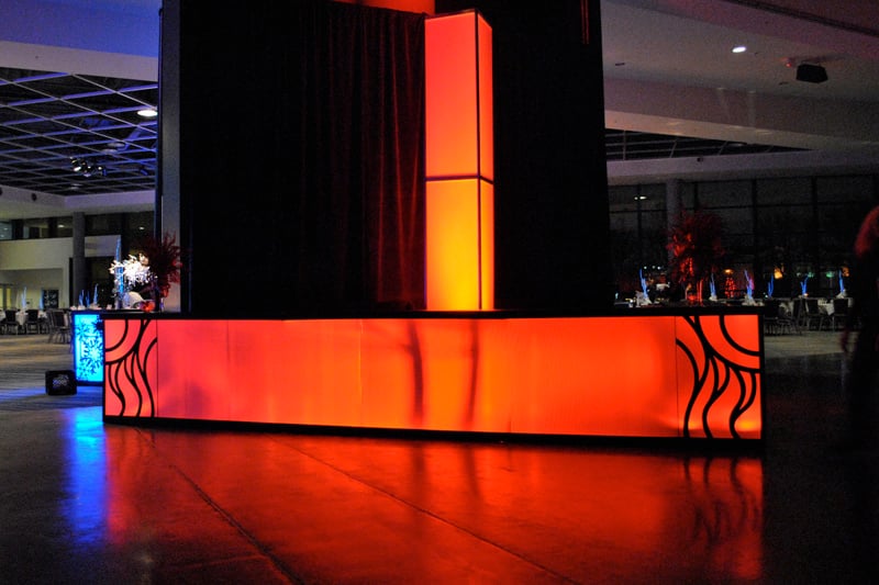 An orange illuminated bar and light column create a focal point for a corporate party.