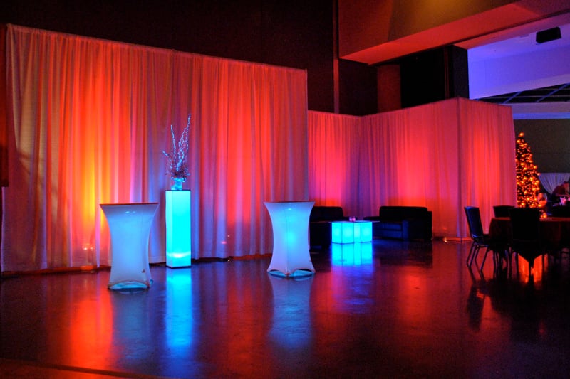 Glowing cocktail tables and lounge seating with warm uplighting against white drapery.