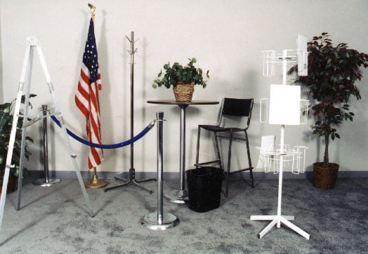 An arrangement of booth accessories including an easel, flag, coat rack, rope stanchions, pedestal table, stool, wastebasket and literature rack.