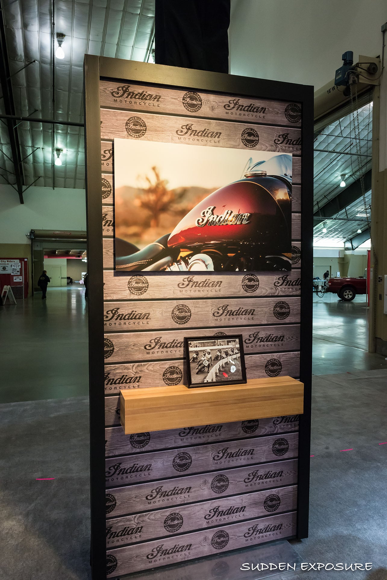 A freestanding Indian Motorcycle display with a wood-style graphic, large photograph and shelf.