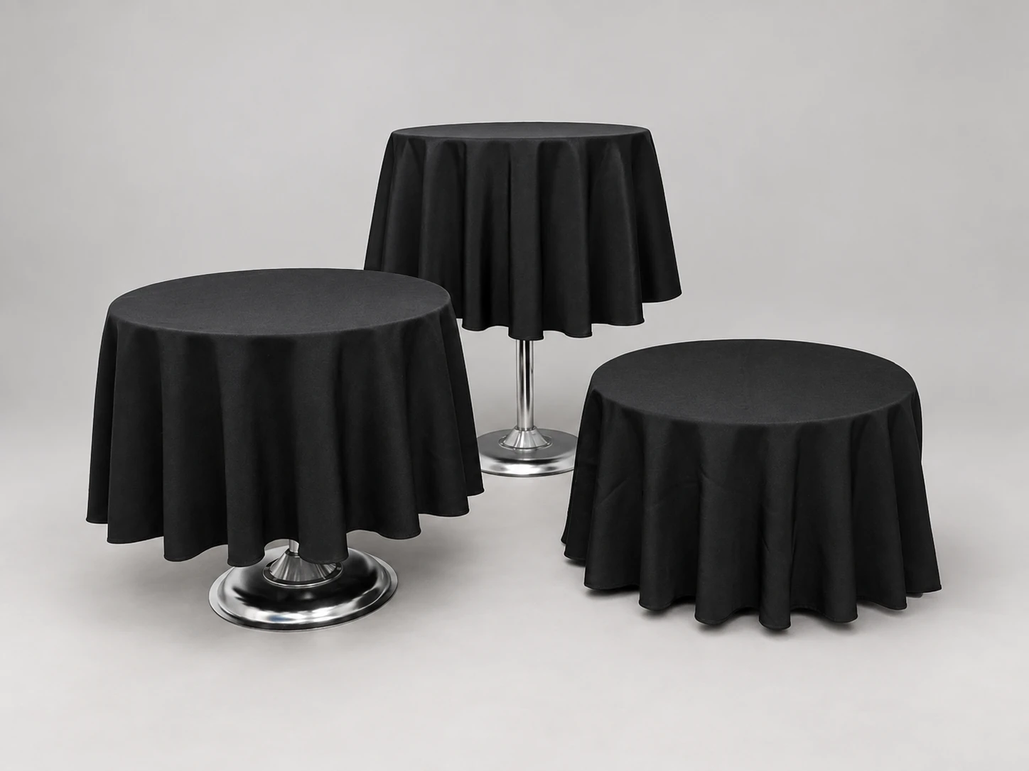 Three round pedestal tables at different heights, with black tablecloths and chrome bases.