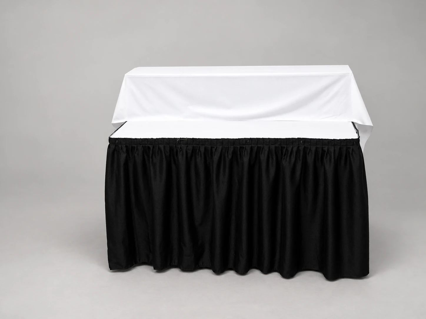 A white-topped display table with one raised rear tier and black table skirting.
