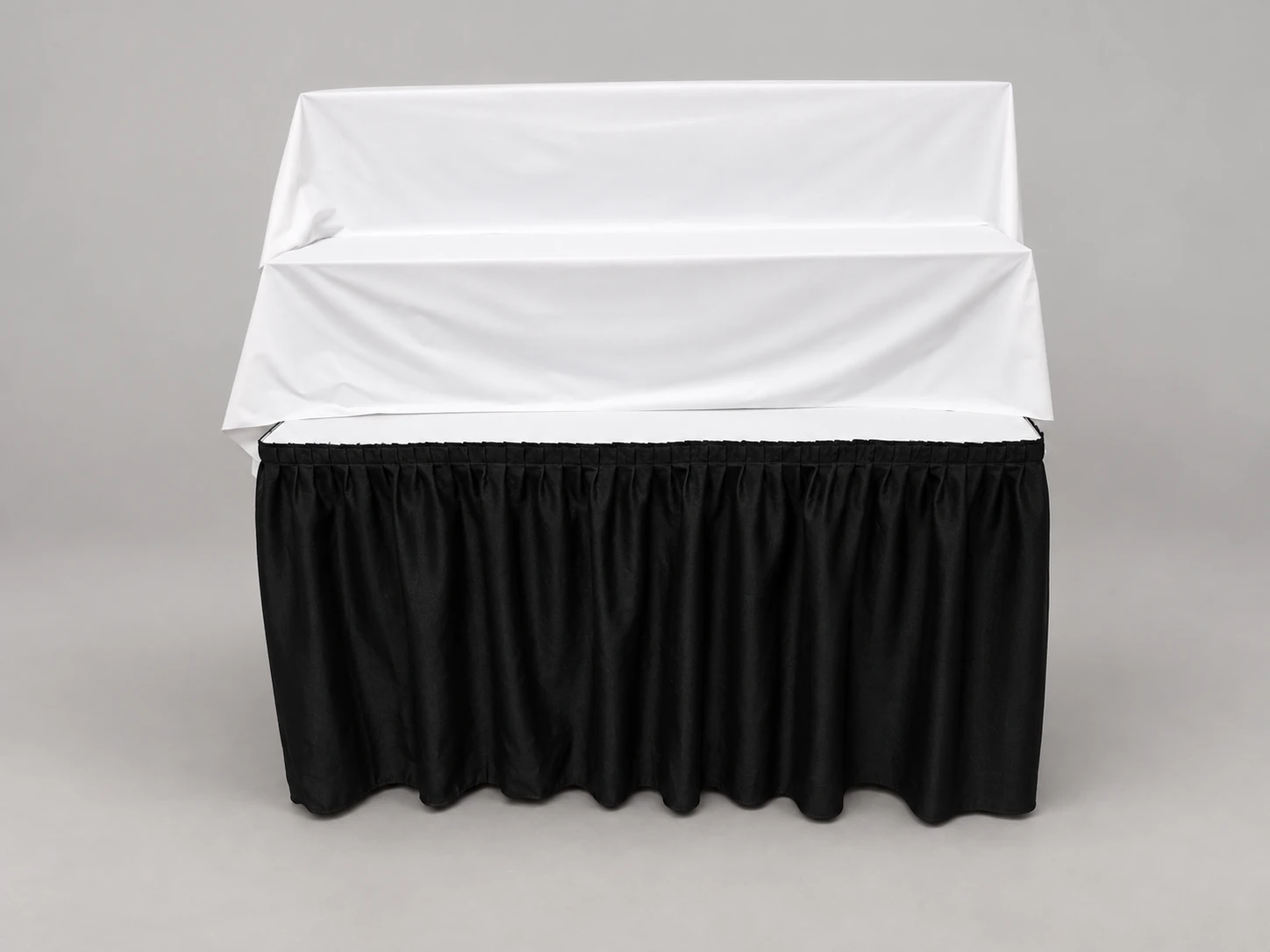 A table with two white-covered raised display tiers and black pleated skirting.